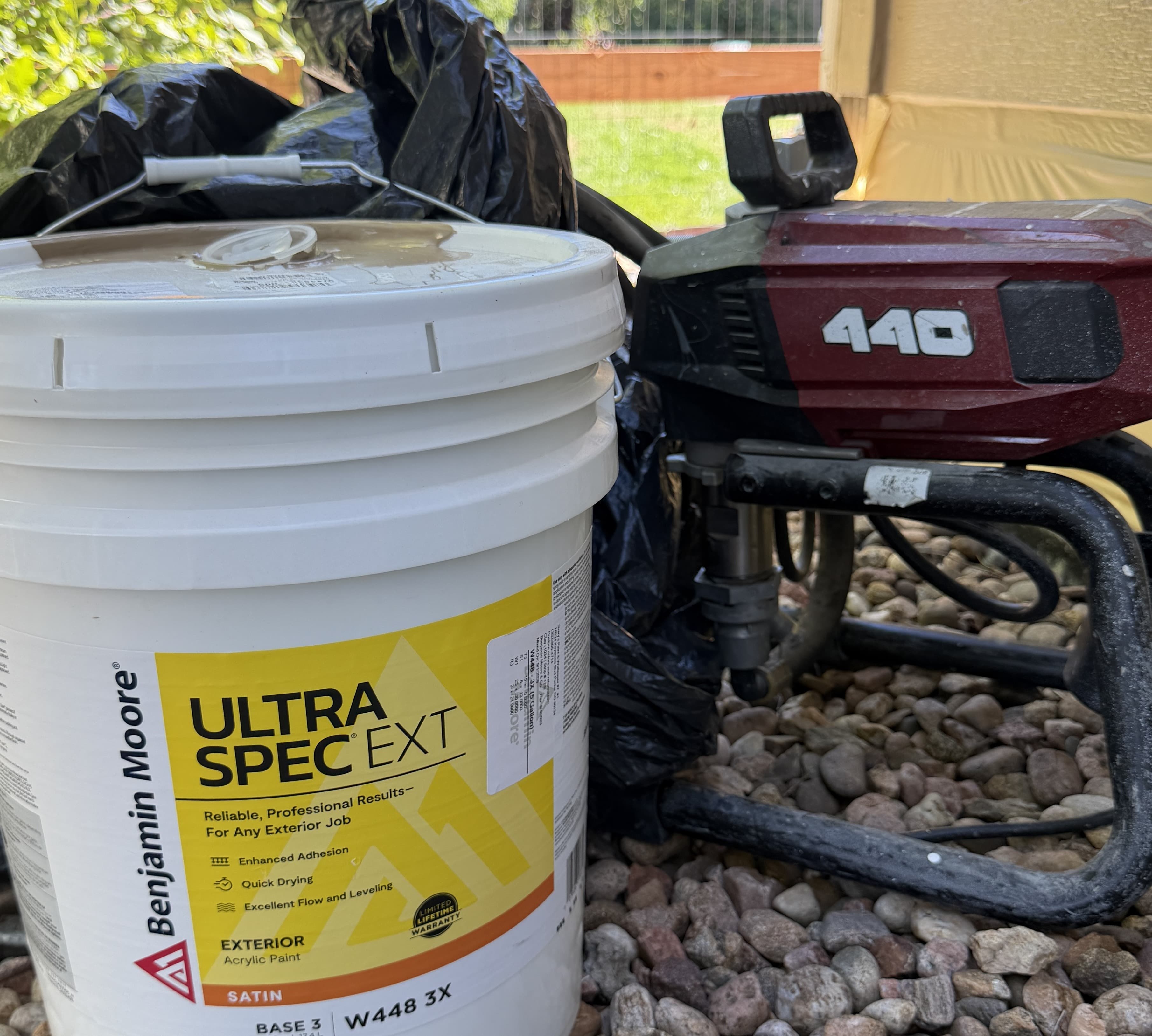 Benjamin Moore Ultra Spec EXT five-gallon bucket and a Titan Impact 440 sprayer on river rock