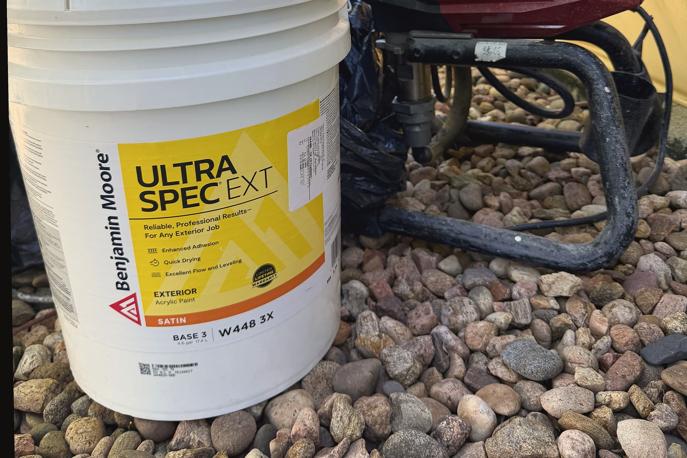 Benjamin Moore Ultra Spec EXT five-gallon bucket and a Titan Impact 440 sprayer on river rock