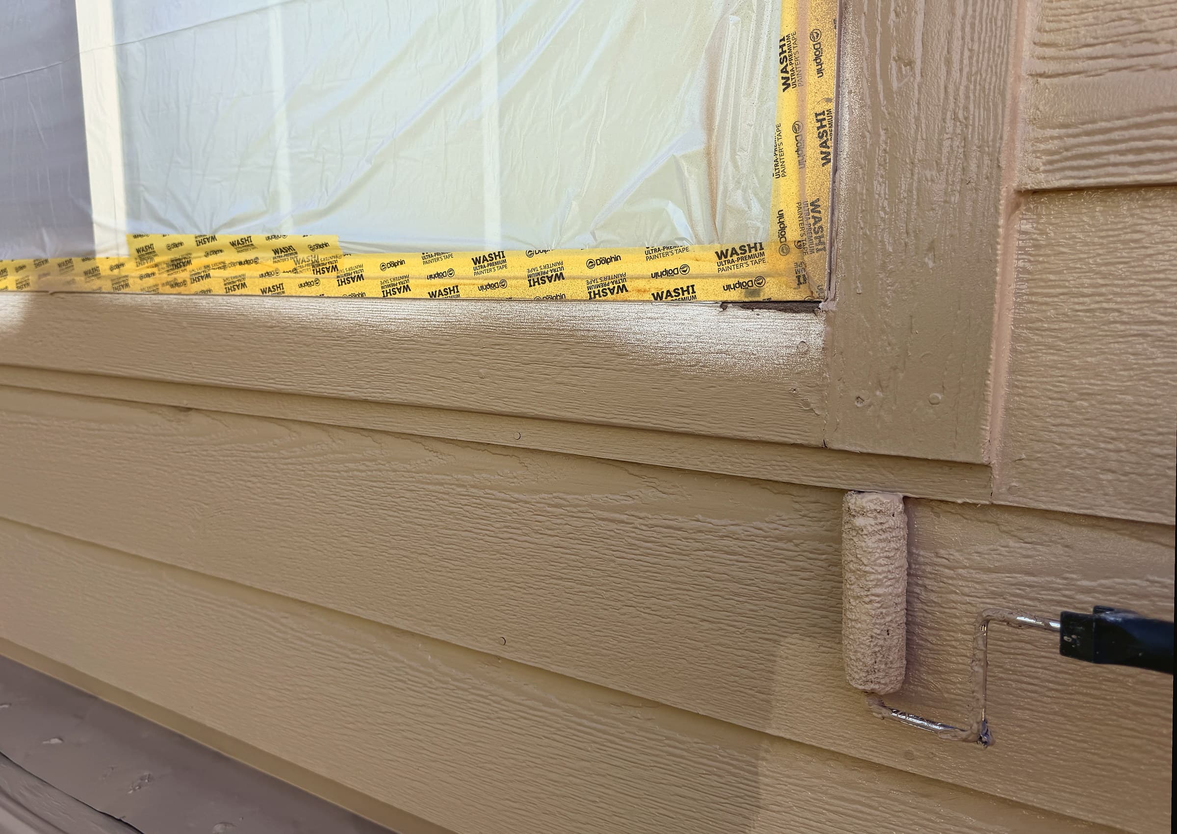 Thick roller coat of tan paint over sprayed lap siding, with the window plastic-masked
